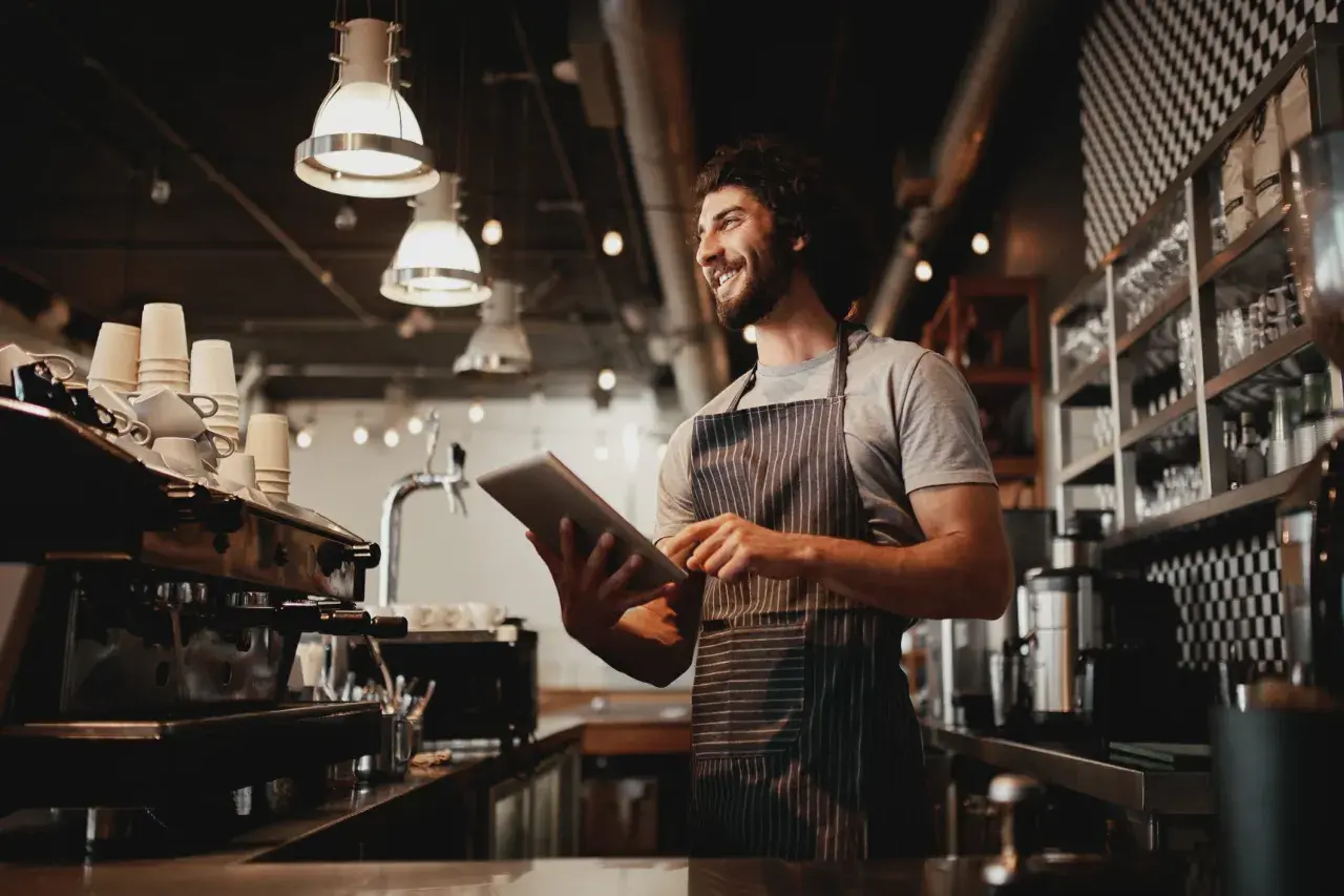 Gerente de un restaurante revisa pedidos en su tableta, sonriendo.