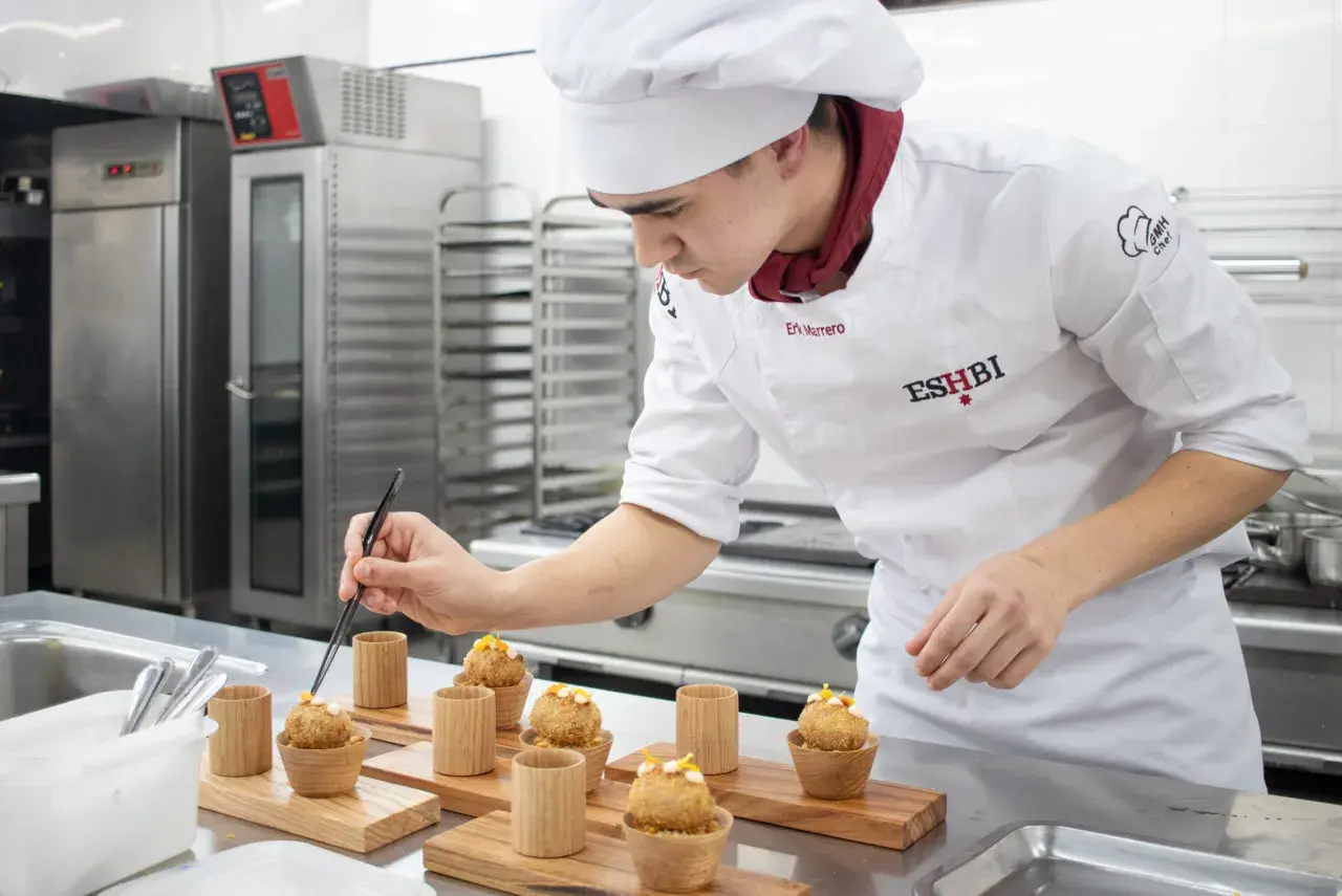 Joven chef perfecciona pequeños bocados, demostrando su dominio en ciencias culinarias y gastronómicas.