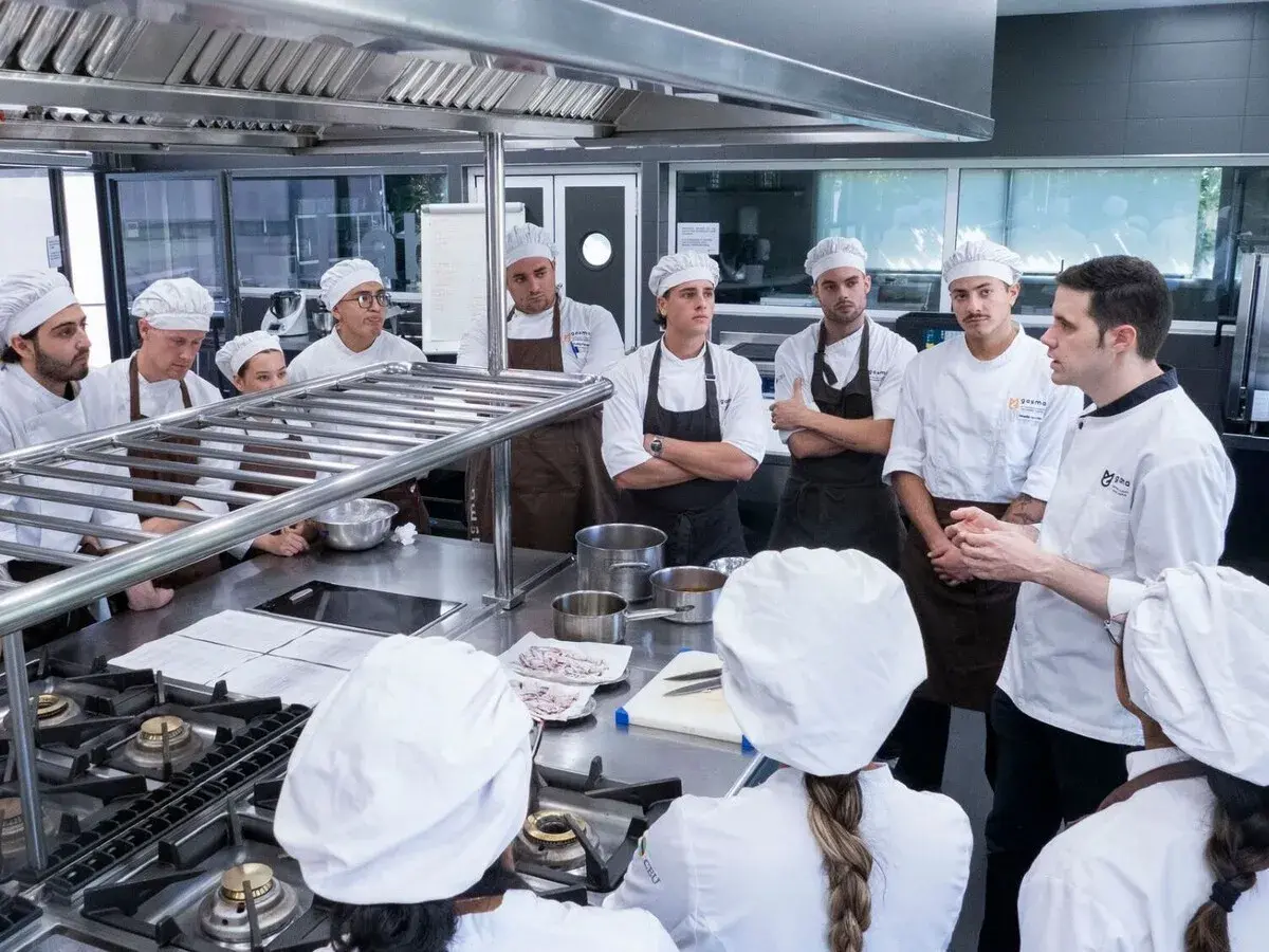 Estudiantes en un curso gestión restaurantes gratis, atentos a las instrucciones de un chef en una cocina profesional.