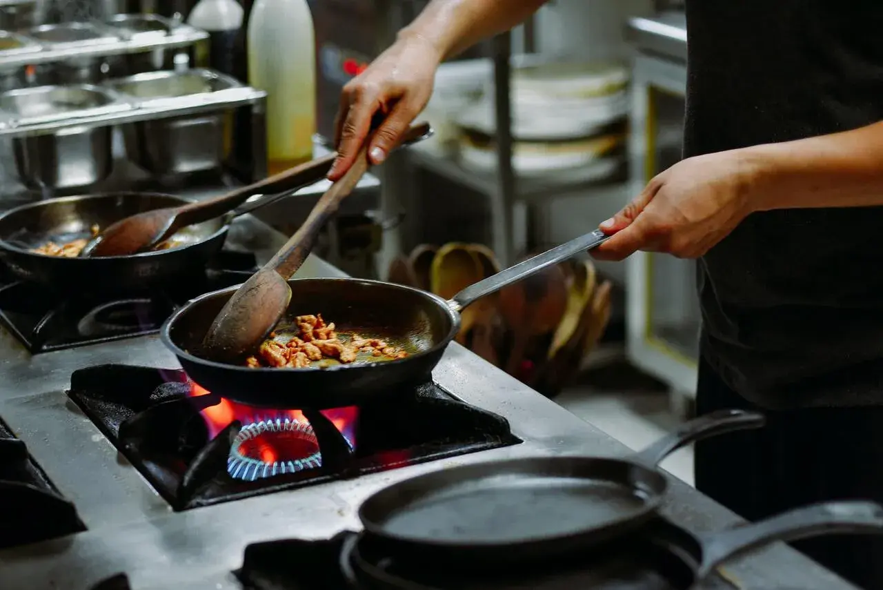 Manos expertas cocinan en sartenes sobre fuego vivo, un arte que se aprende en las mejores escuelas de cocina en España.