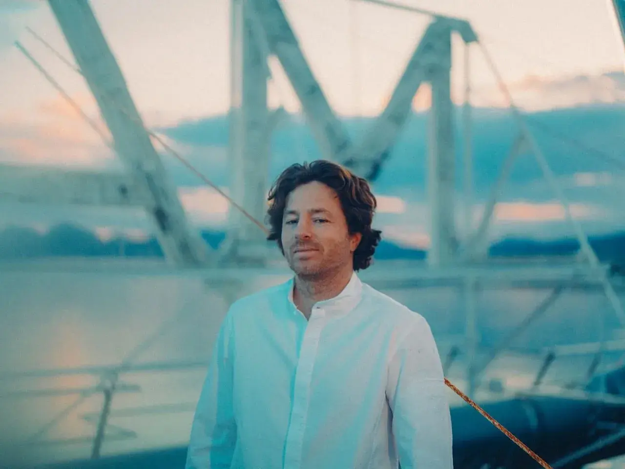 Jean Imbert, con camisa blanca, posa frente a una estructura de barco al atardecer.