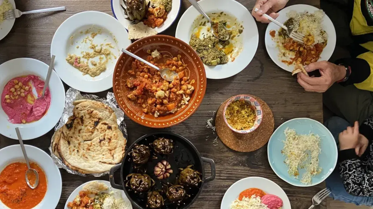 Mesa llena de platos variados, perfectos para recetas de cenas con amigos. Hummus, garbanzos, alcachofas y pan pita.