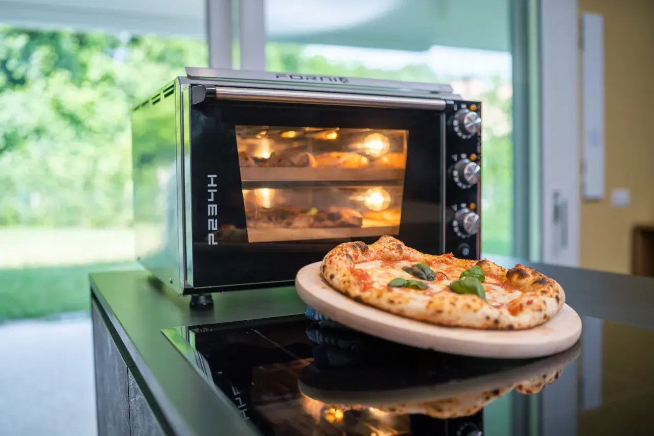 Horno eléctrico con dos pizzas dentro, una lista para disfrutar y otra en proceso. El tiempo de cocción de una pizza en horno eléctrico es clave para su textura.