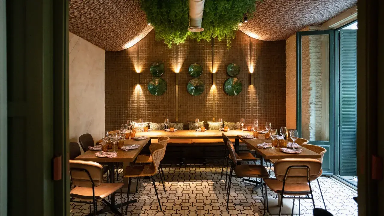 Elegante diseño de iluminación en restaurantes, con mesas puestas y vegetación colgante.