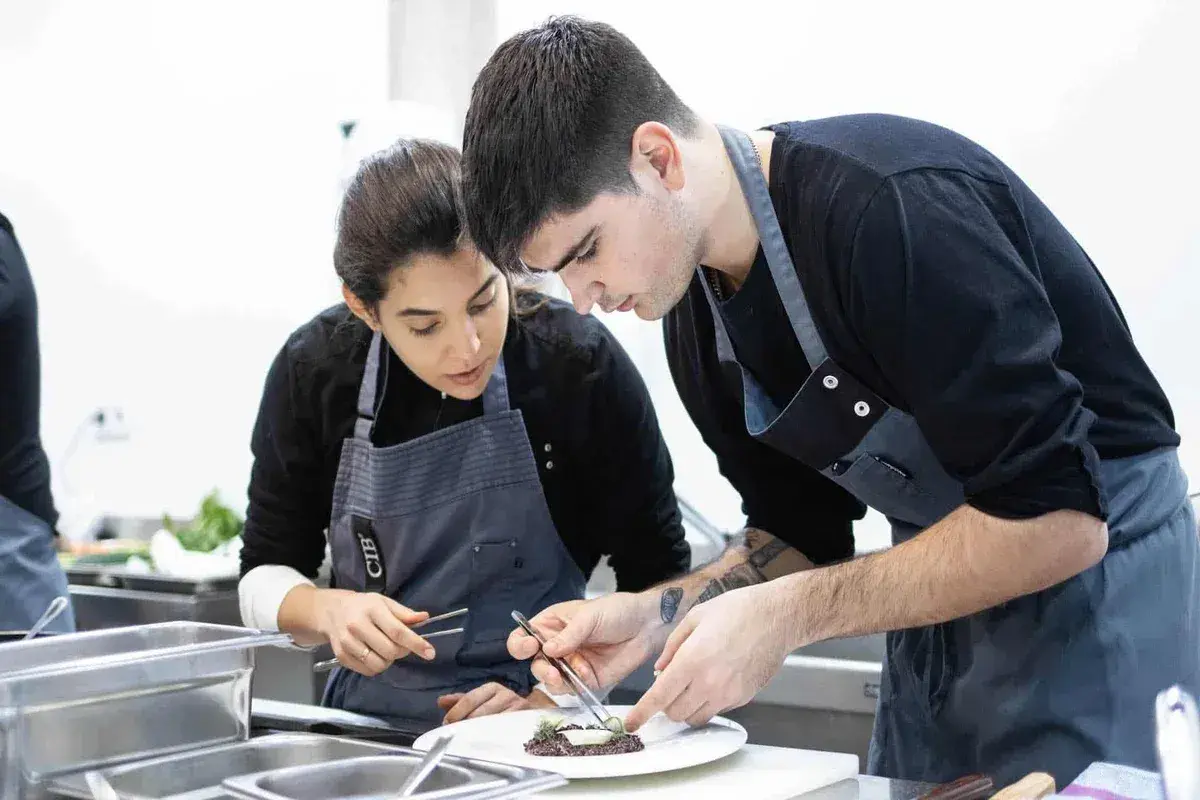 Dos aprendices de cocina, concentrados en emplatar un plato, aprendiendo como ser chef.