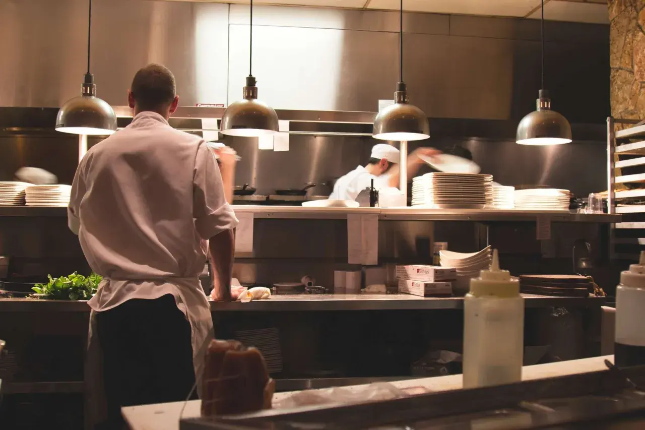 Un ayudante de cocina en España prepara ingredientes frescos en una cocina profesional, con pilas de platos y utensilios listos para el servicio.