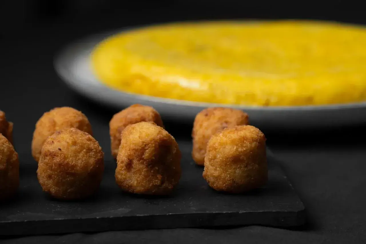 Croquetas doradas y crujientes, un ejemplo de que es la quinta gama hostelería, con una tortilla española al fondo.