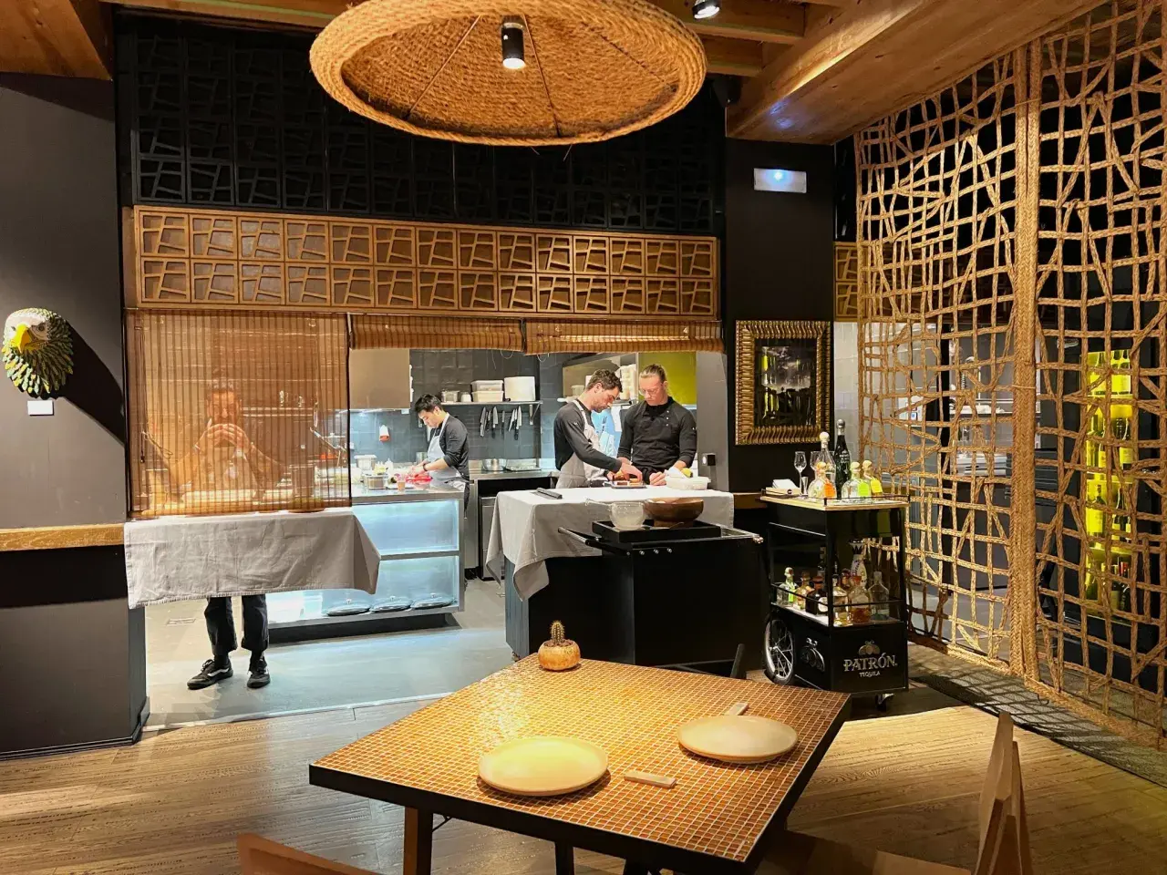 Chefs trabajan en la cocina de un restaurante. Se ve una mesa puesta y un carrito de bebidas. ¡Qué ganas de comer como Paco Méndez!