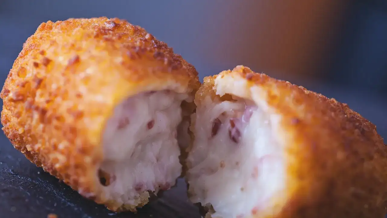 Croqueta dorada y crujiente, partida por la mitad, revelando un interior cremoso. La proporción de harina y leche para croquetas es clave para esta textura.