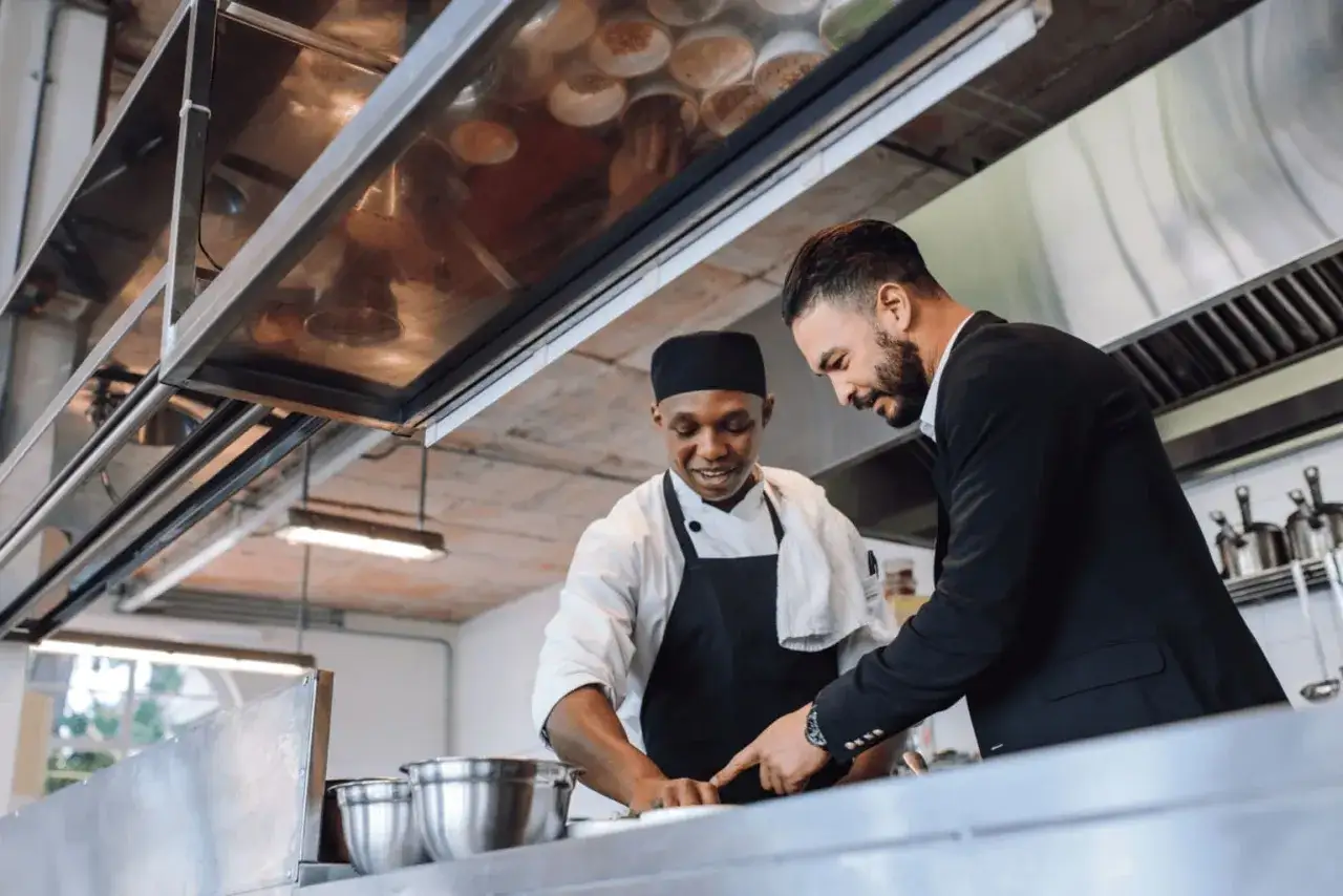 El gerente de un restaurante revisa el trabajo de un chef en la cocina.