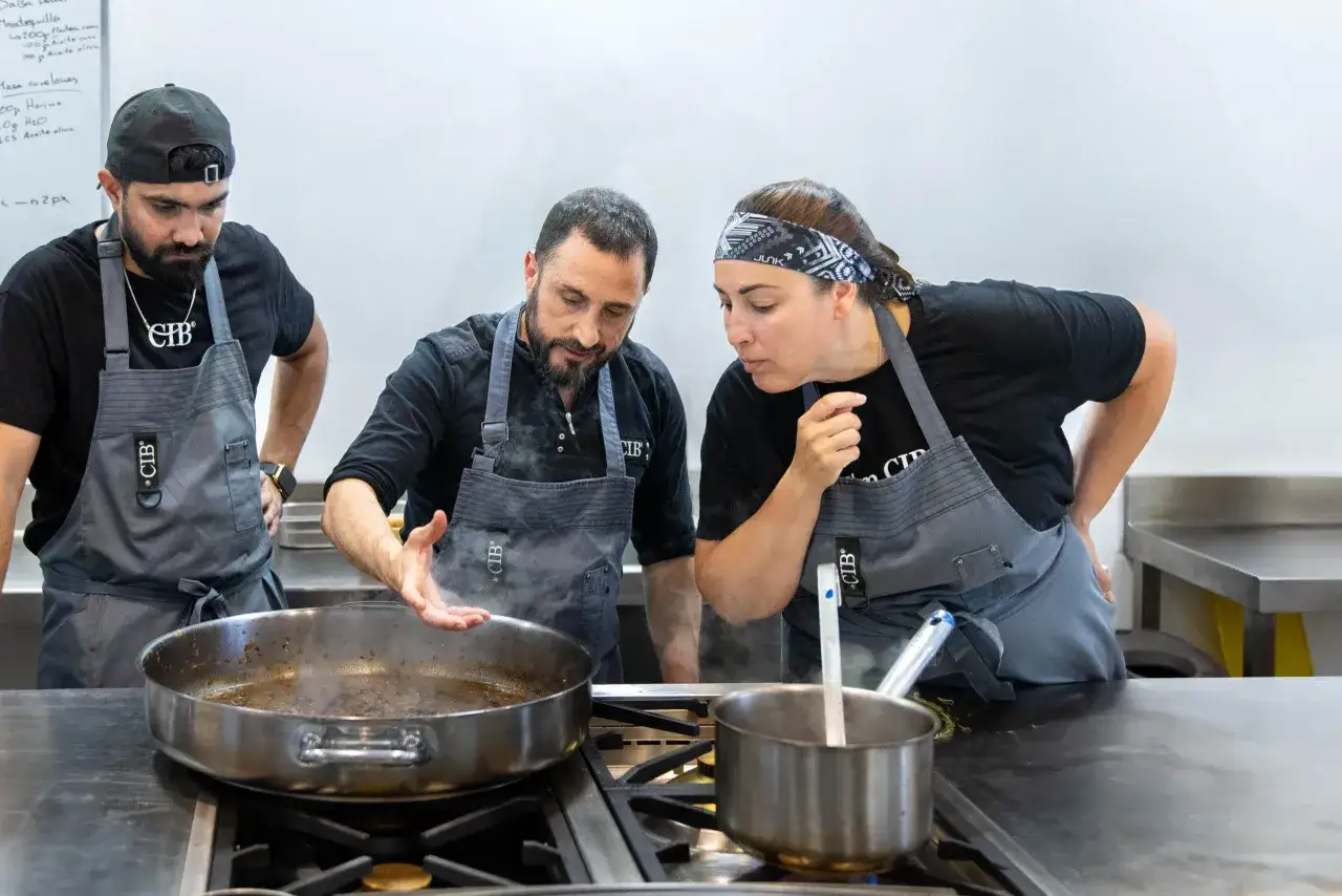 Tres chefs observan atentamente una sart&eacute;n humeante, evaluando el tiempo de cocci&oacute;n.