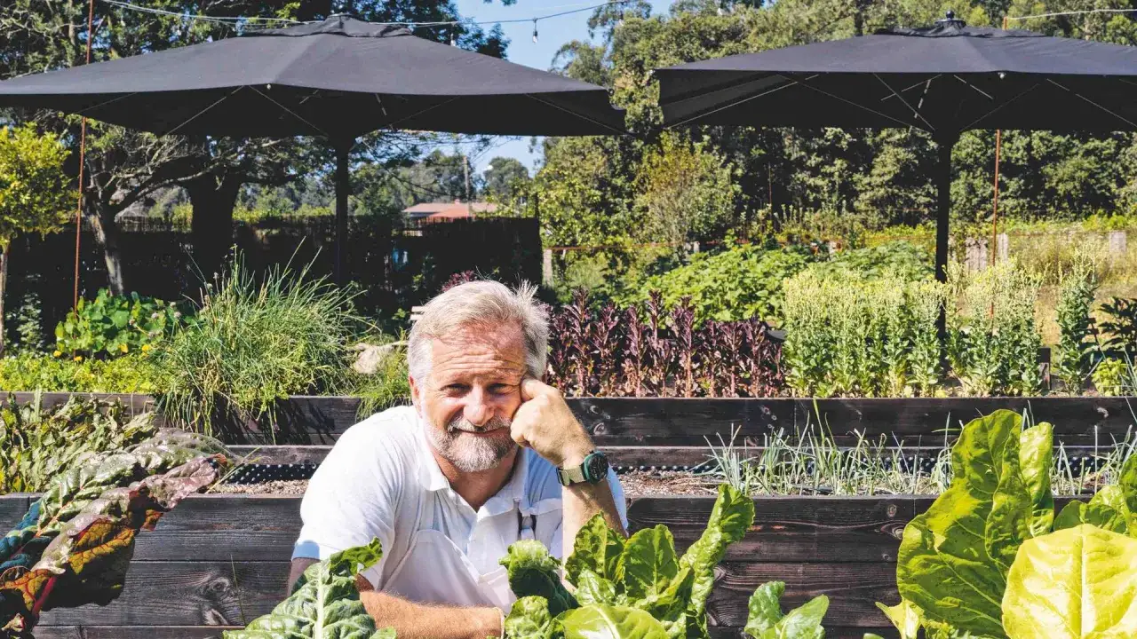 Chef sonriente en su huerto, rodeado de verduras frescas, con la promesa de una estrella verde Michelin en cada plato.