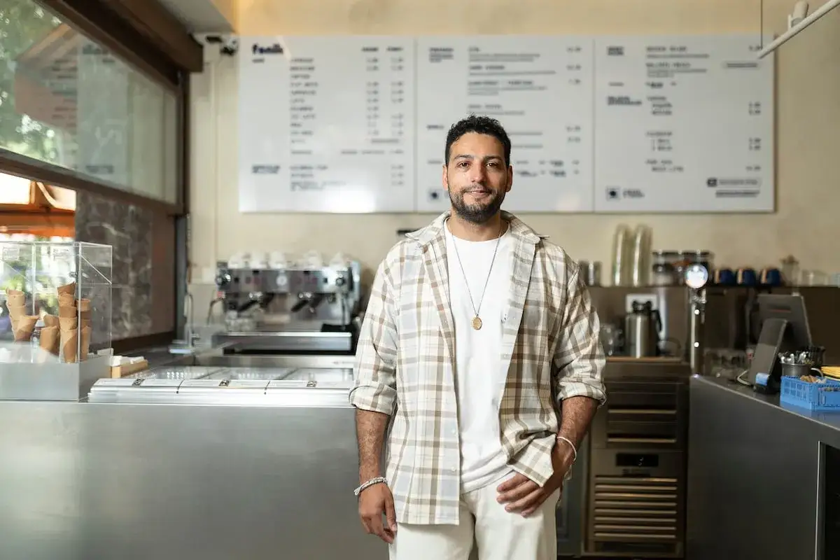 Hombre sonriente en helader&iacute;a, con men&uacute; y m&aacute;quina de caf&eacute;. Un lugar ideal para compartir en redes sociales restaurantes.