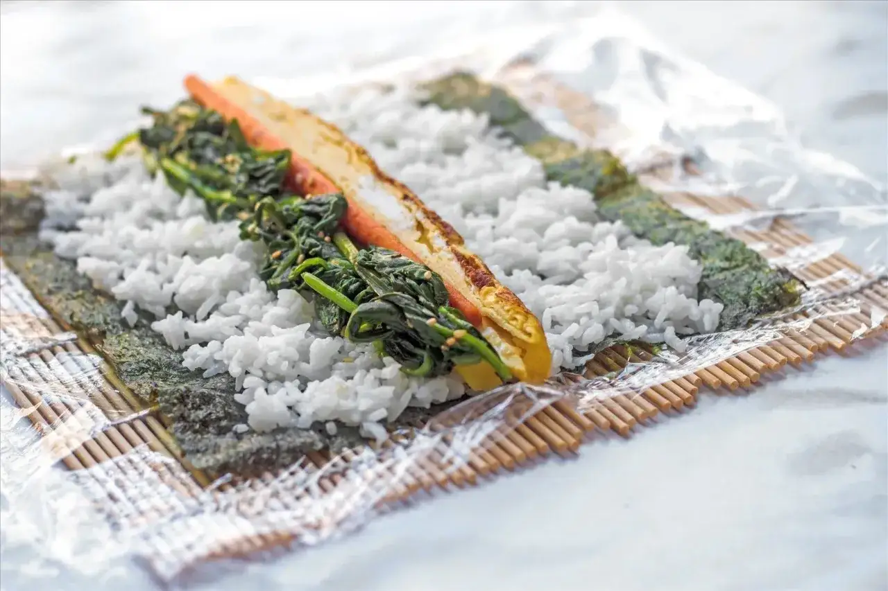 Arroz, nori y espinacas sobre una esterilla de bamb&uacute;, mostrando c&oacute;mo se hace el sushi.