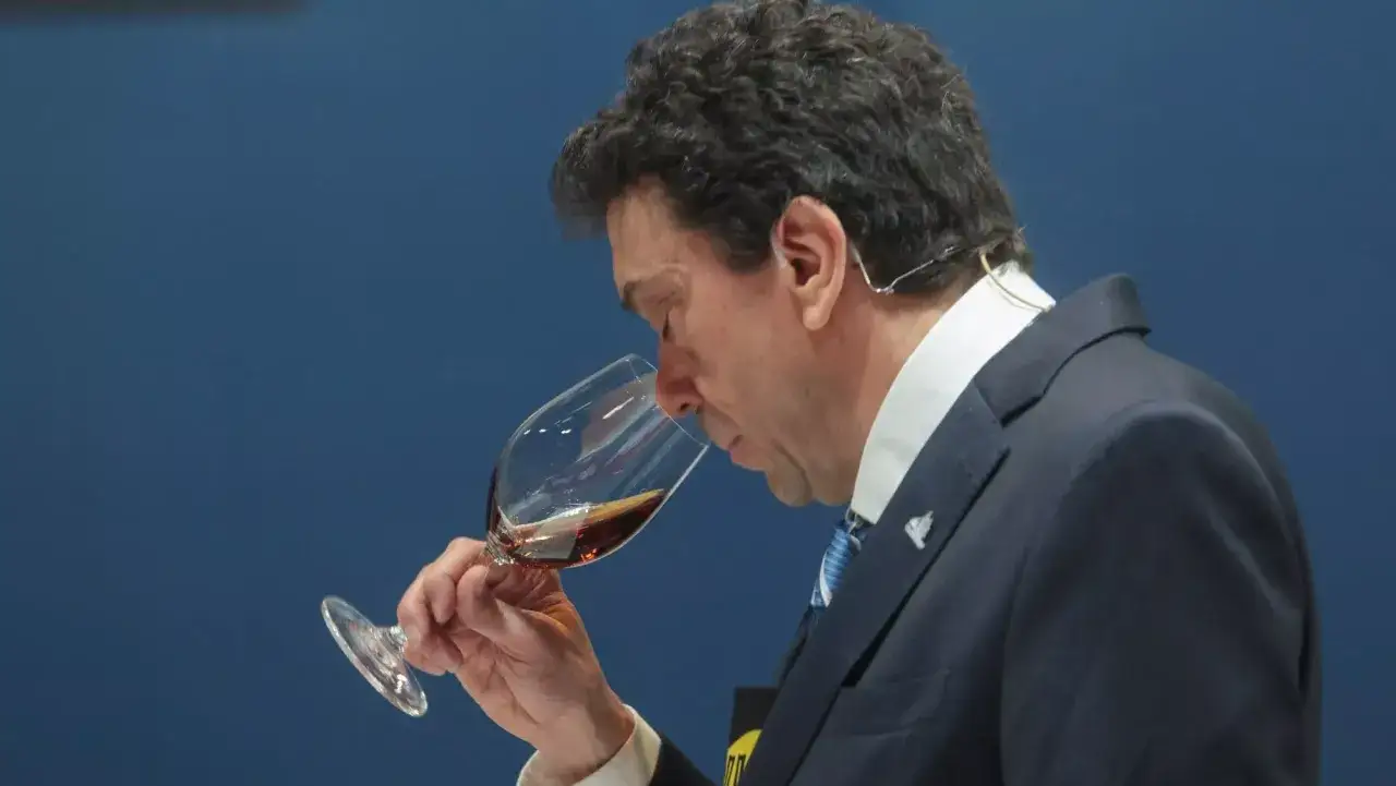 Hombre con traje y corbata azul huele un vino tinto en una copa, aprendiendo como ser sommelier.