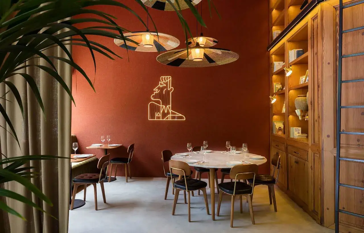 Diseño de restaurante con paredes terracota, lámparas de mimbre, un letrero de neón y estanterías de madera.