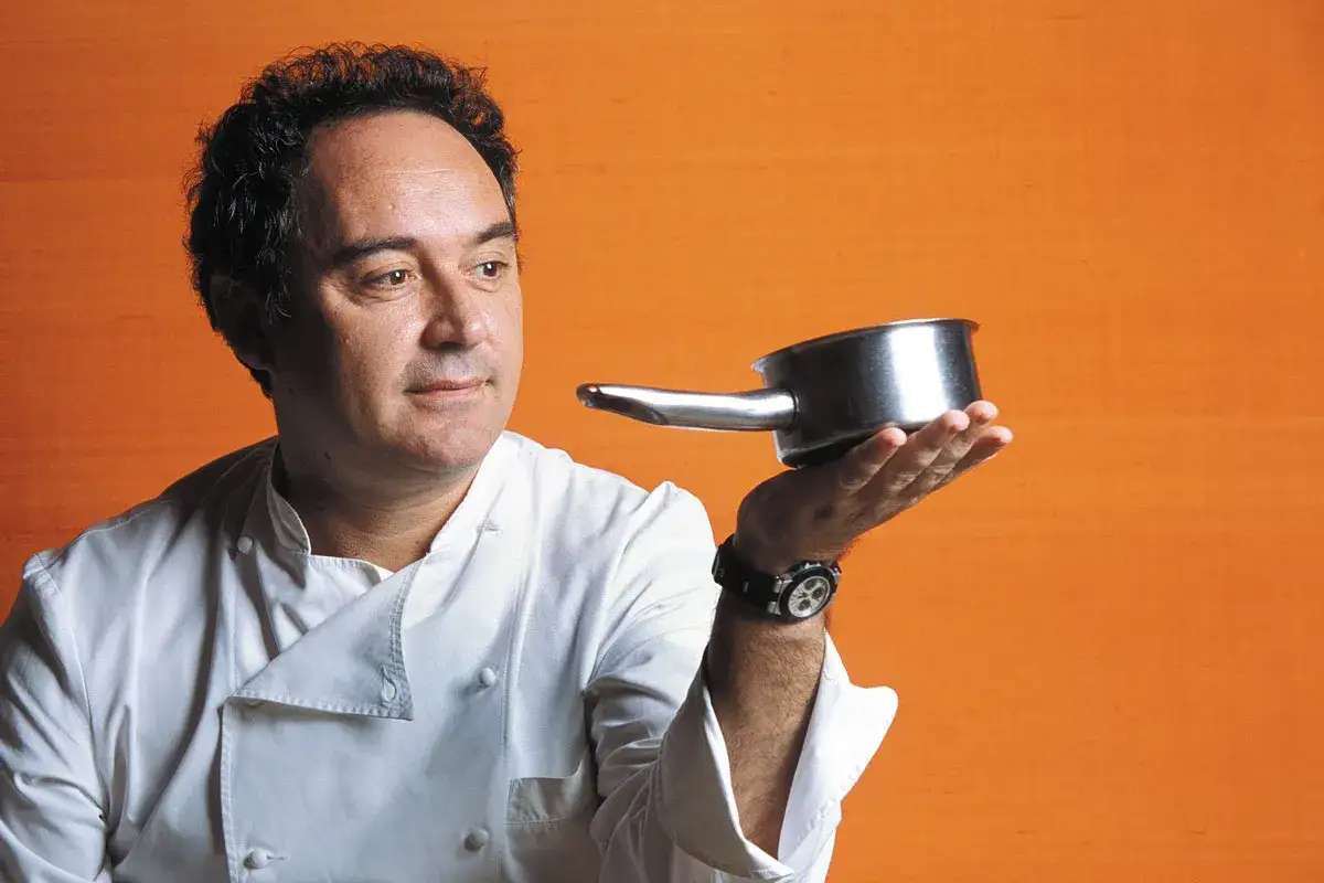 Chef catal&aacute;n con estrellas Michelin, con una cazuela en la mano, sobre fondo naranja.