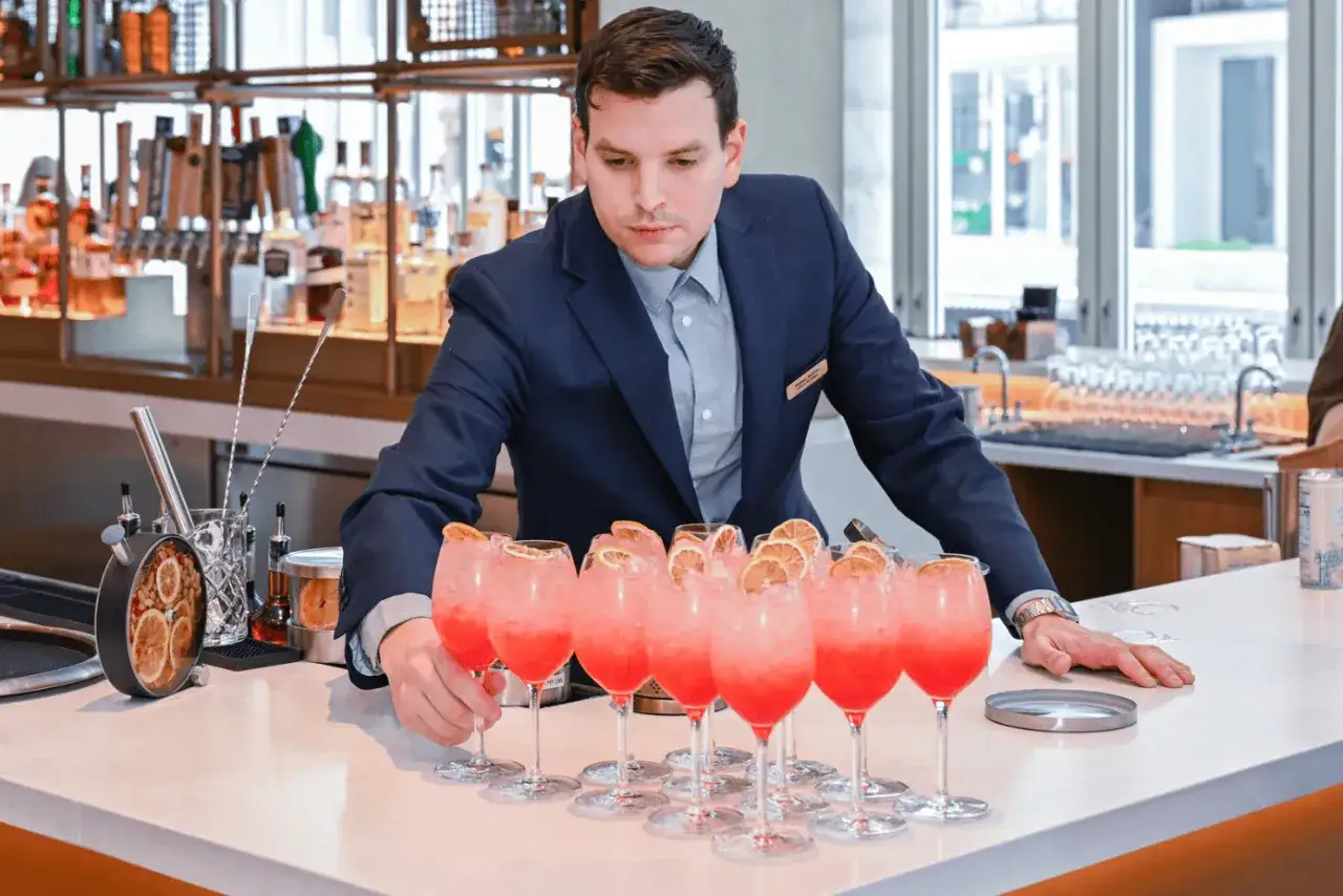El director de alimentos y bebidas supervisa c&oacute;cteles rosados con rodajas de naranja en una barra.