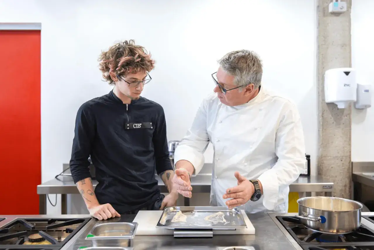 Un chef experimentado explica una t&eacute;cnica a un joven aprendiz. El convenio jefe de cocina se refleja en la transmisi&oacute;n de conocimientos.