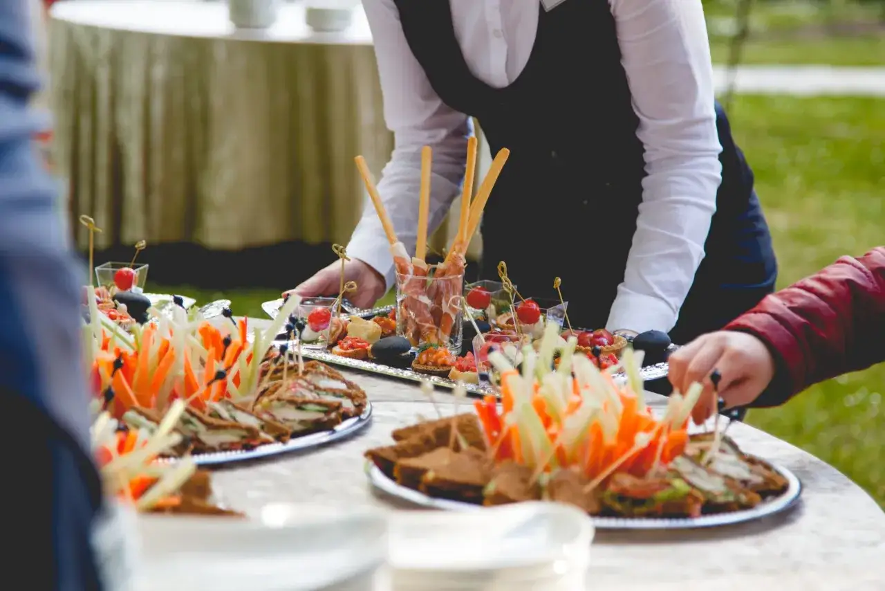 Camarero sirviendo canap&eacute;s y s&aacute;ndwiches, mostrando varios tipos de servicios en restaurantes para un evento al aire libre.