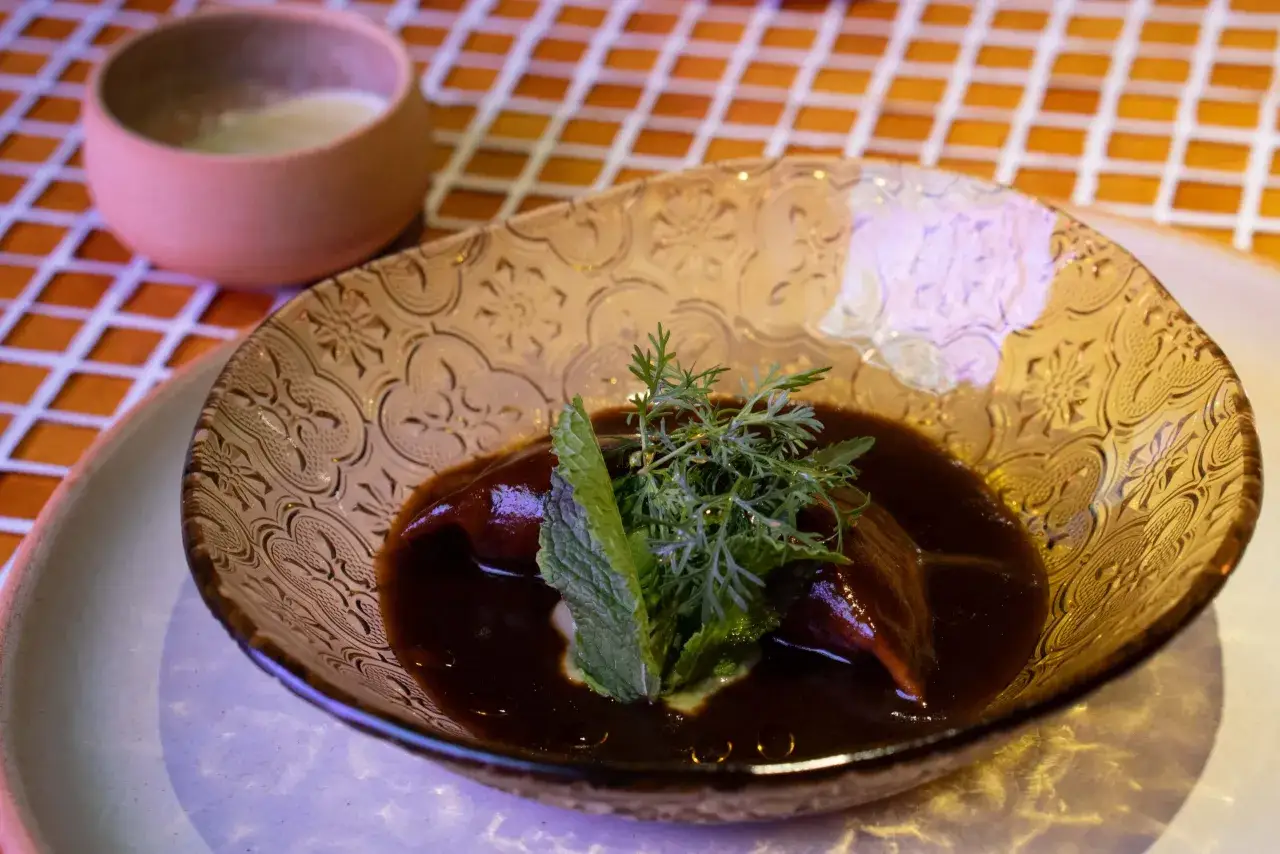 Plato de mole oscuro con hierbas frescas, servido en un cuenco de cristal labrado. &iexcl;Un sabor que te har&aacute; decir 