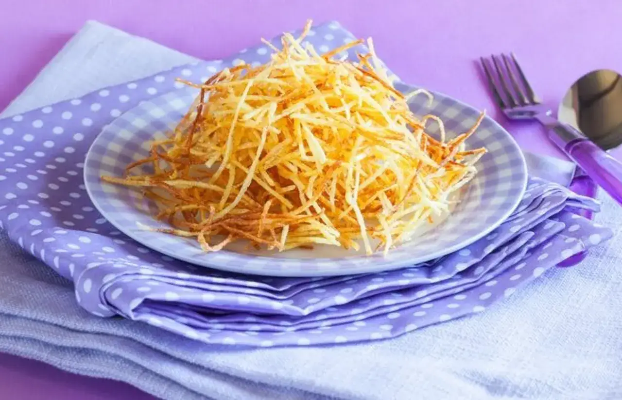 Patatas paja crujientes en un plato a cuadros, listas para servir. Aprende como cortar patatas paja perfectas.