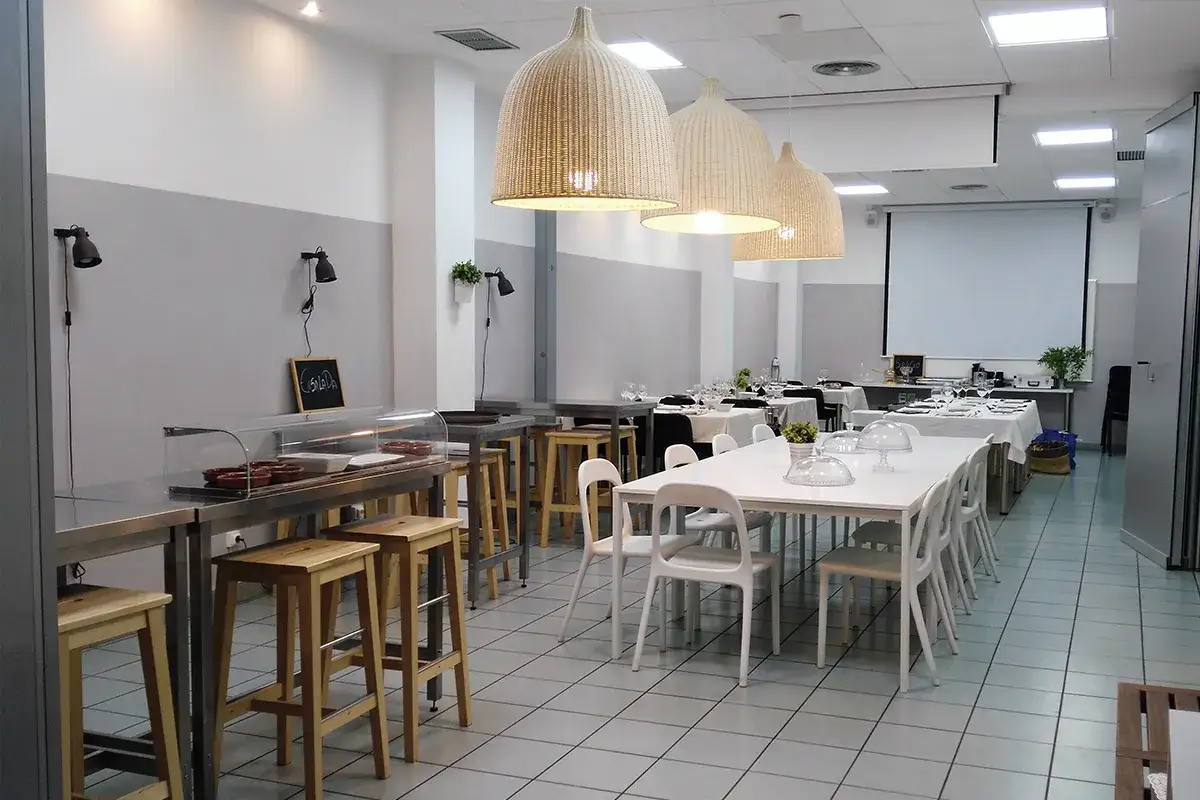 Salón preparado para un curso de gestión de restaurante, con mesas, sillas y una vitrina expositora.