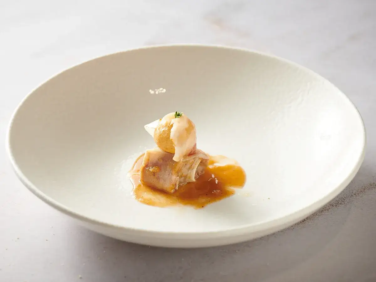 Delicado plato estrella michelin: rollo de carne con salsa dorada y una esfera cremosa coronada con hierbas.