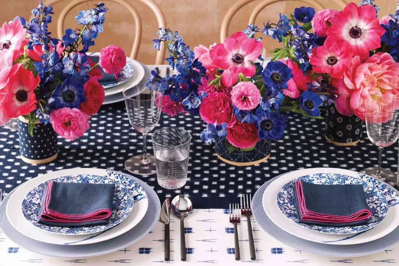 Mesa puesta con flores vibrantes y vajilla azul y blanca. Se aprecian varios tipos de tenedores, listos para una cena elegante.