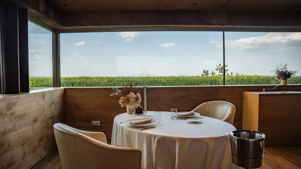 Mesa elegante en un restaurante estrella Michelin, con vistas a un campo verde bajo un cielo azul.