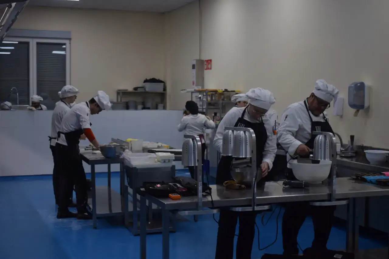 Estudiantes de ciencias culinarias y gastronómicas practican en una cocina profesional, preparando ingredientes y usando batidoras.