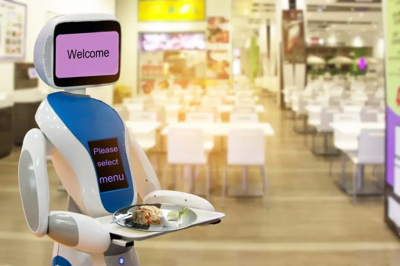 Robot que sirve comida en un restaurante futurista. En su pantalla se lee 