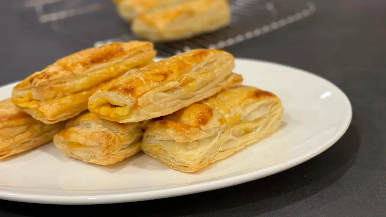 Deliciosos pastelitos de hojaldre dorados en un plato blanco. Descubre qué hacer para que el hojaldre no se ablande y mantenga su crujiente textura.