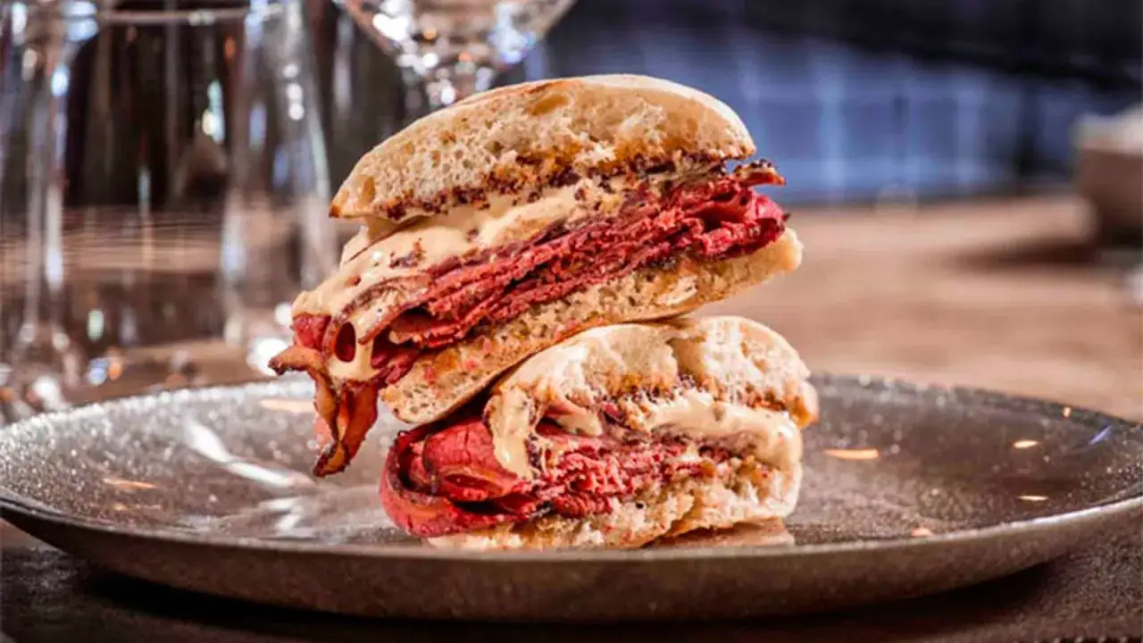Mollete de pastrami generosamente relleno, apilado en un plato oscuro, listo para ser devorado.