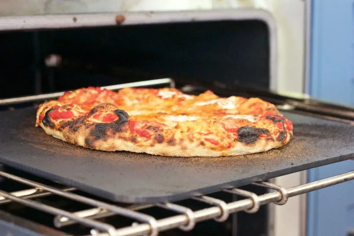 Pizza reci&eacute;n salida del horno, con bordes dorados y burbujeantes. La temperatura y el tiempo perfectos para una pizza deliciosa.