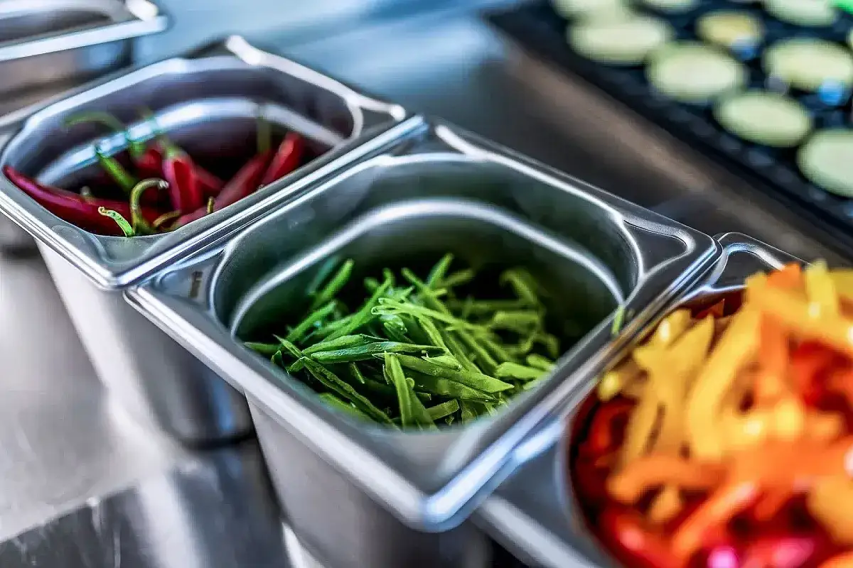 Contenedores de acero inoxidable con pimientos rojos, judías verdes y pimientos de colores, listos para ser usados como entremetier en cocina.