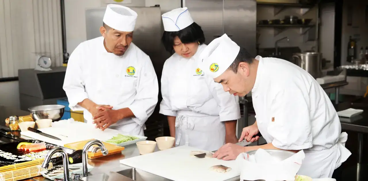 Chefs en un curso de cocina japonesa preparan pescado y vegetales.