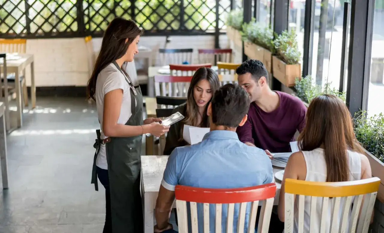 Una mesera sonriente, que es personal de sala, atiende a una pareja en un restaurante.
