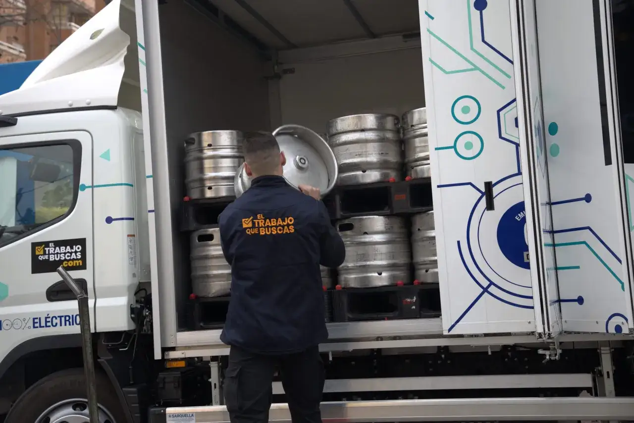 Hombre descarga barriles de cerveza de un camión eléctrico, parte de la cadena de suministro del canal horeca.