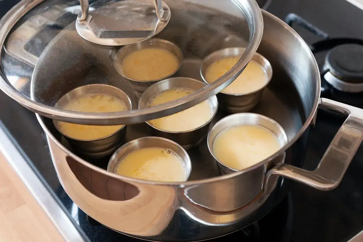 Varios moldes con postre cremoso se cocinan al vapor en un ba&ntilde;o mar&iacute;a.