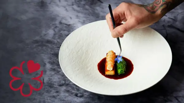Un chef 3 estrellas Michelin decora un plato con langosta, brócoli y una flor azul.