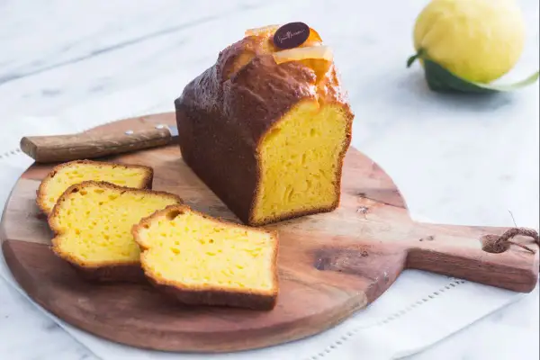 Un delicioso plumcake de limón, recién cortado, con rodajas esponjosas y un limón fresco al fondo.
