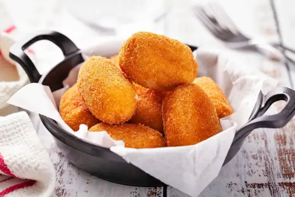 Croquetas doradas y crujientes en una sartén negra, listas para disfrutar.
