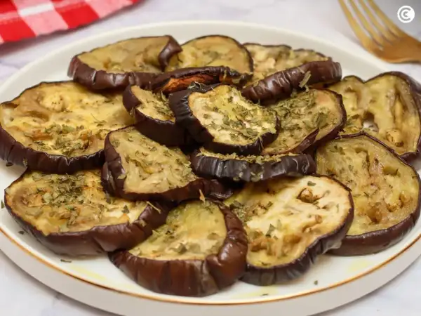Rodajas de berenjena asada, tiernas y doradas, espolvoreadas con hierbas aromáticas. Un plato sencillo y delicioso para disfrutar del sabor de las berenjenas.