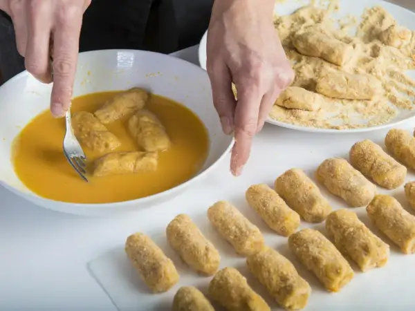 Manos rebozando croquetas en huevo. Se puede congelar la masa de croquetas para freír después.