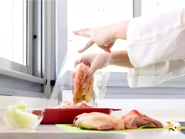 Manos con guantes introducen pollo en una bolsa para cocina al vacío.
