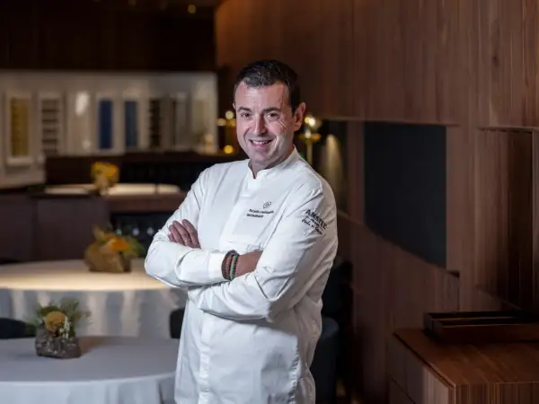 Chef sonriente en su cocina, con el logo de Ricard Camarena Restaurantes en su uniforme.