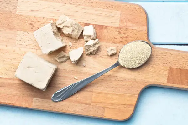 Bloques de levadura fresca y una cuchara con levadura seca granulada sobre una tabla de cortar. Se puede congelar la levadura fresca para conservarla.