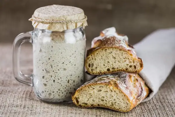 Masa madre burbujeante en un frasco junto a pan recién horneado. La clave para un buen pan está en el tiempo y temperatura para hornear pan.
