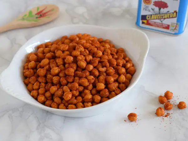 Un tazón blanco lleno de garbanzos fritos crujientes, sazonados con especias rojizas.